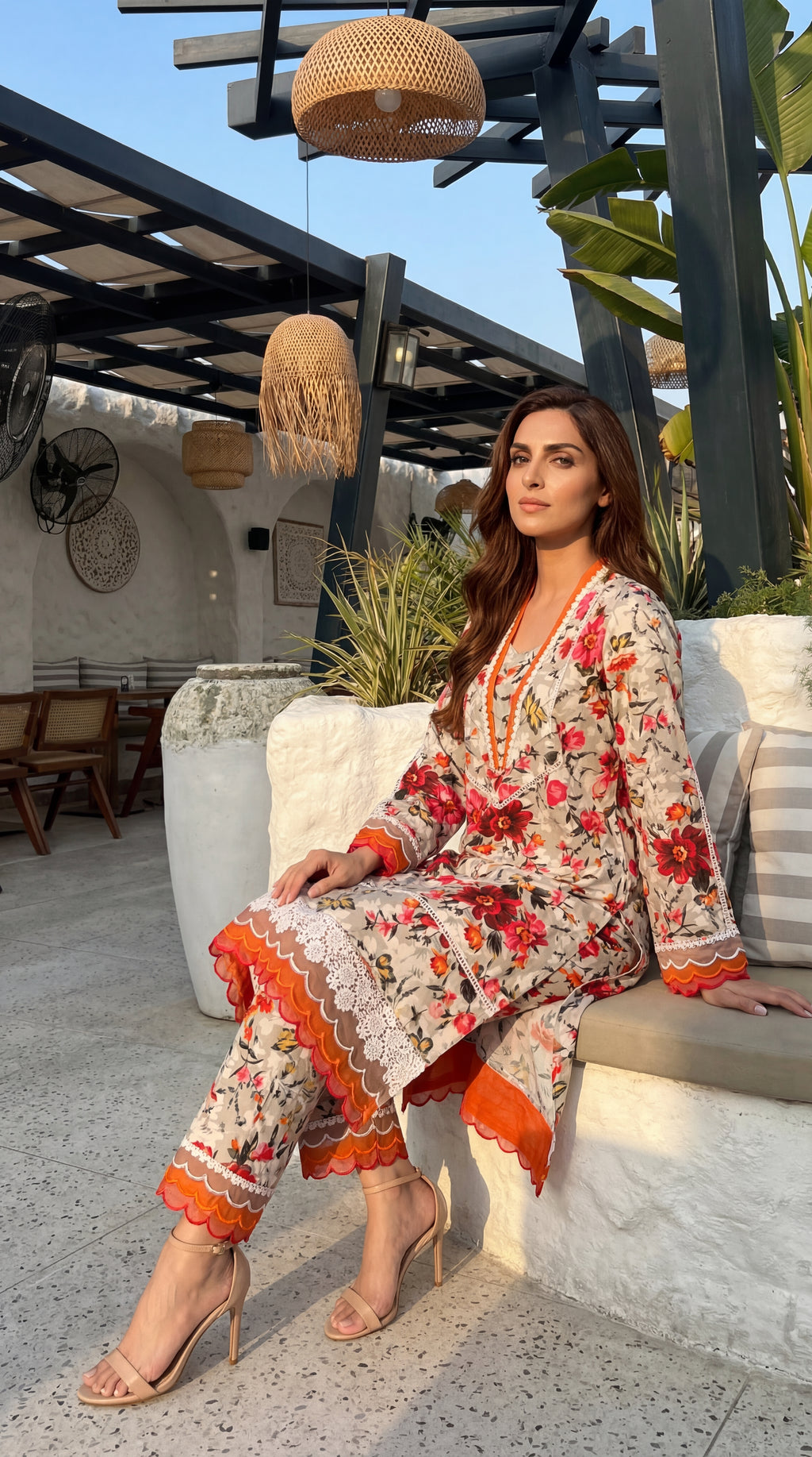 Woman in a floral outfit sitting outdoors with plants and furniture in the background