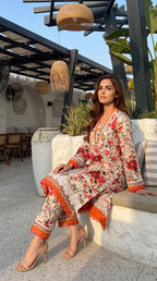Woman in a floral outfit sitting outdoors with plants and furniture in the background