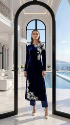 Woman in a navy dress with white floral embroidery standing in a modern interior with a pool view.