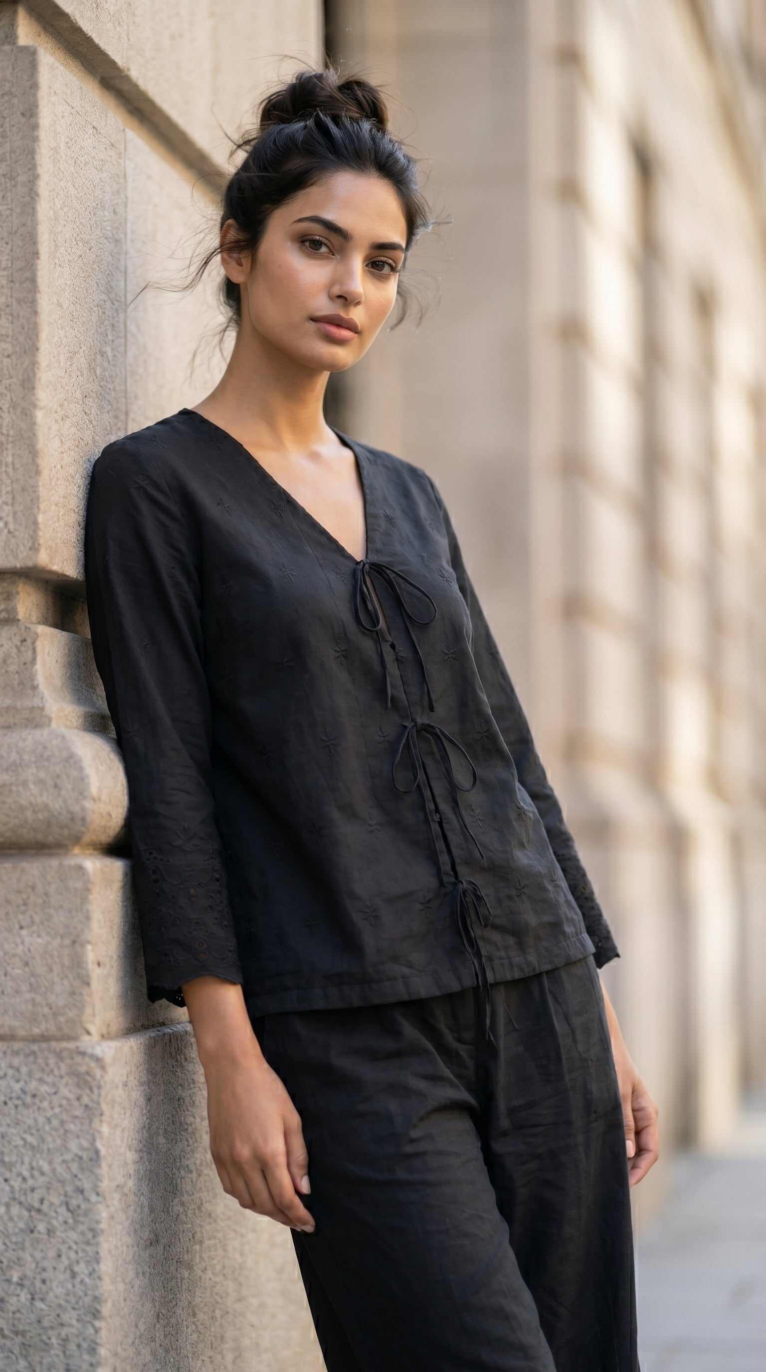 Woman wearing a black outfit leaning against a stone wall.