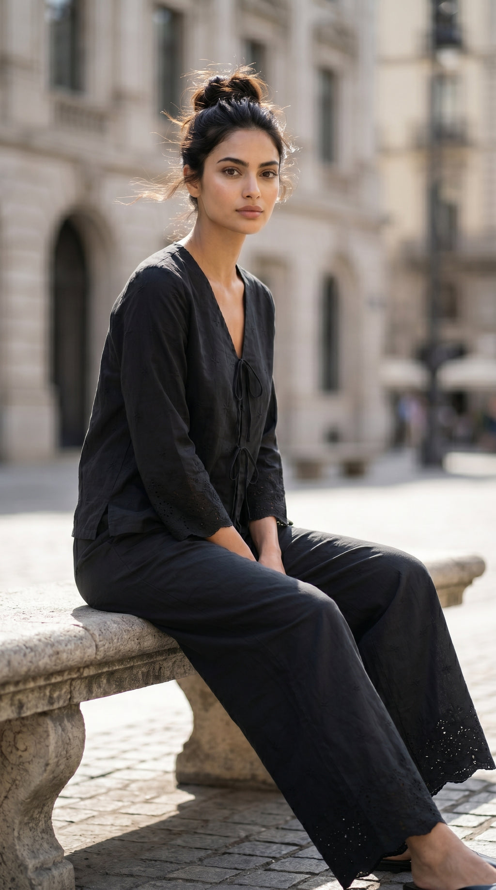 Woman in black outfit sitting on a stone bench in an urban setting