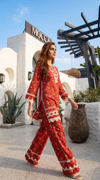 Woman in a red patterned outfit walking outdoors with a building and plants in the background.