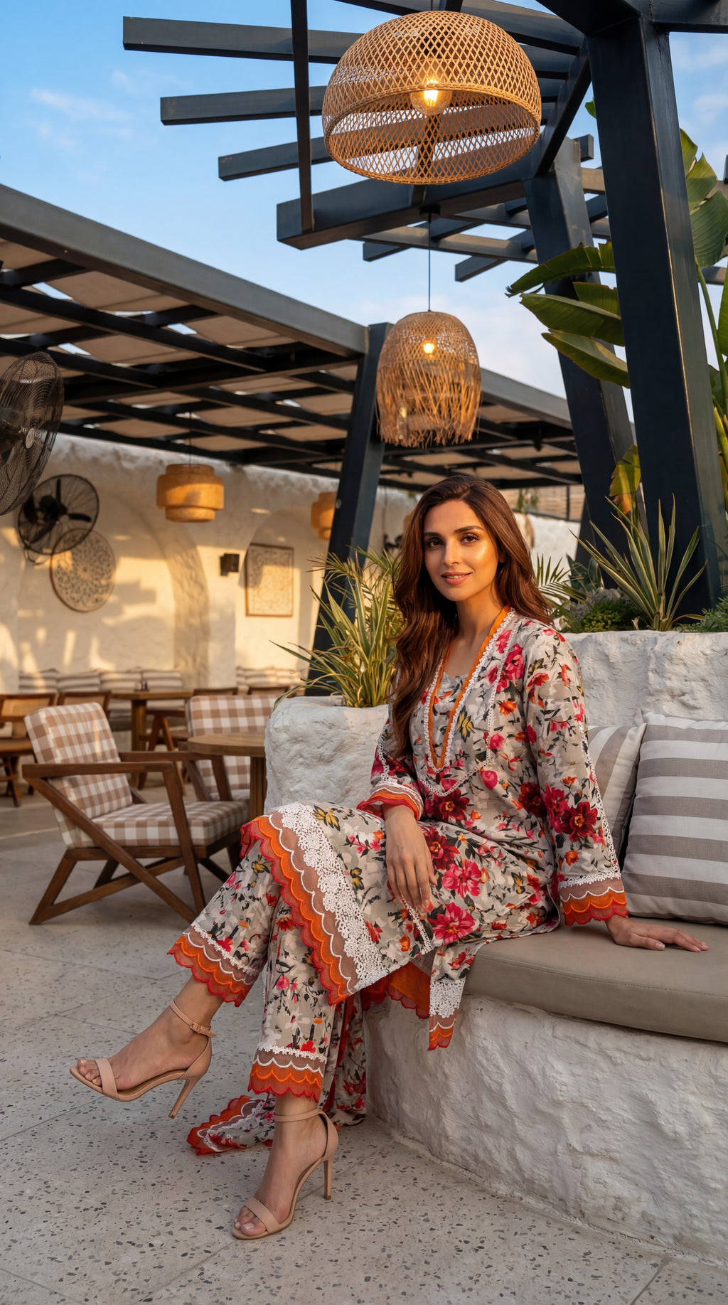 Woman in a floral outfit sitting on a patio with outdoor furniture and plants.