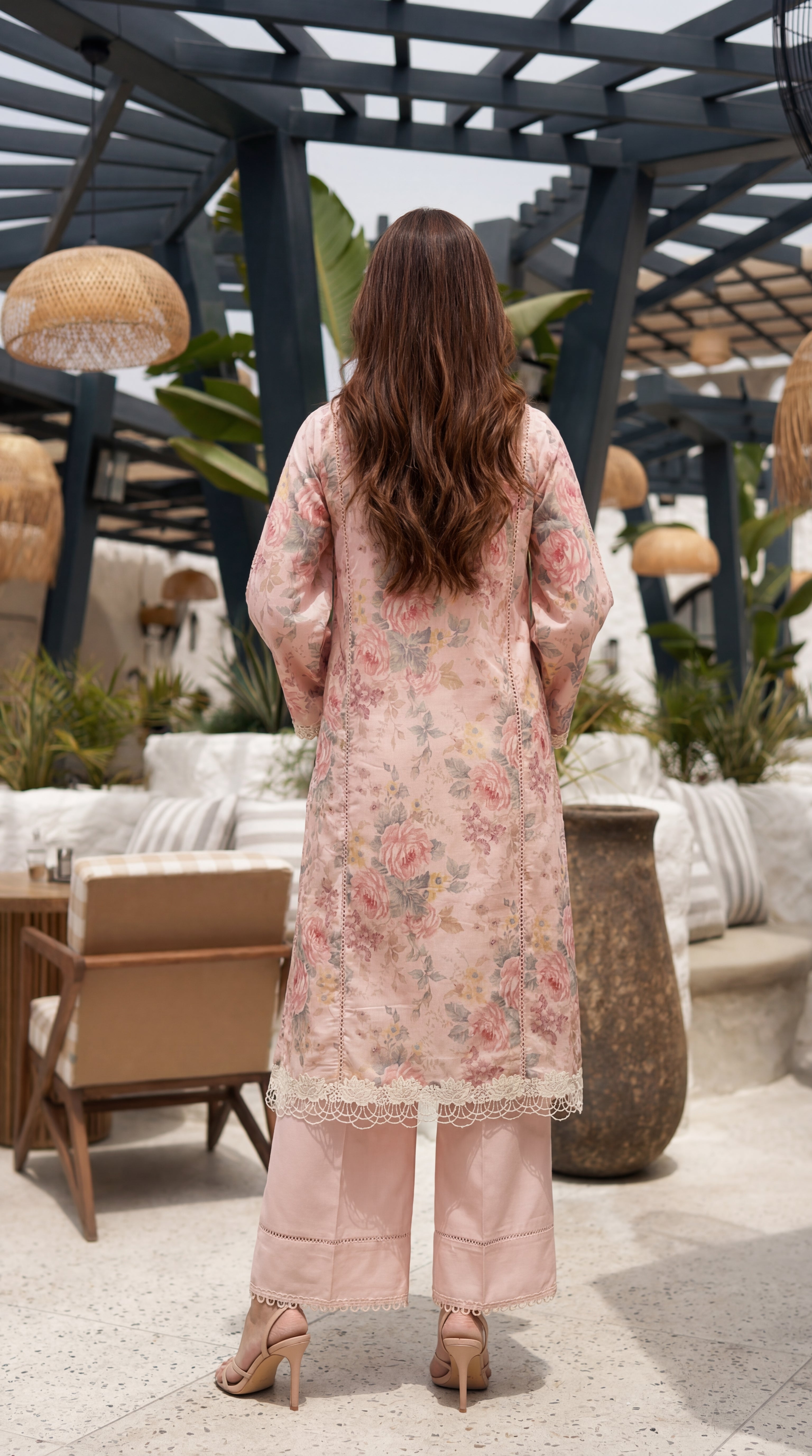 Woman in a floral dress standing in an outdoor setting with plants and furniture.