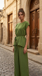 Woman in a green outfit standing in front of an ornate wooden door.