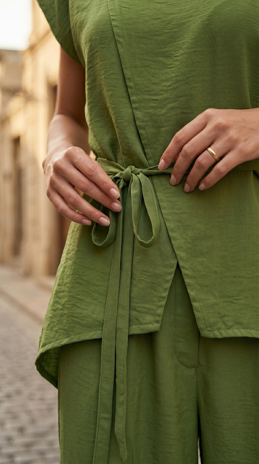 Person wearing a green outfit with a belt, standing on a street.
