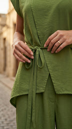 Person wearing a green outfit with a belt, standing on a street.