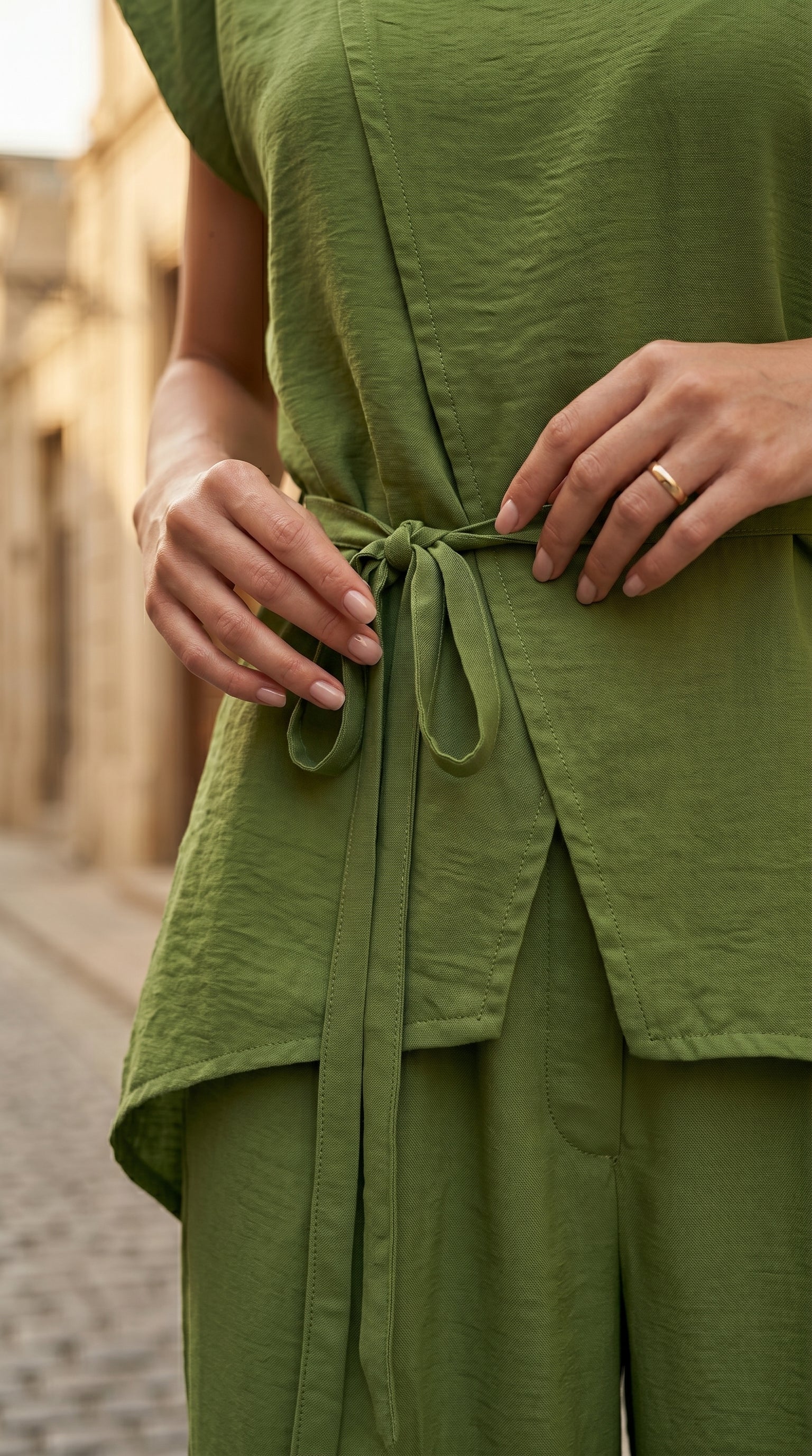 Person wearing a green outfit with a belt, standing on a street.