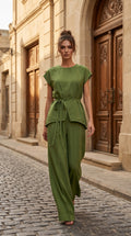Woman in a green outfit standing on a cobblestone street with a building in the background