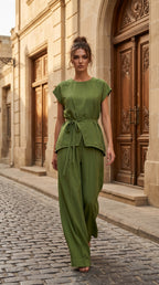 Woman in a green outfit standing on a cobblestone street with a building in the background