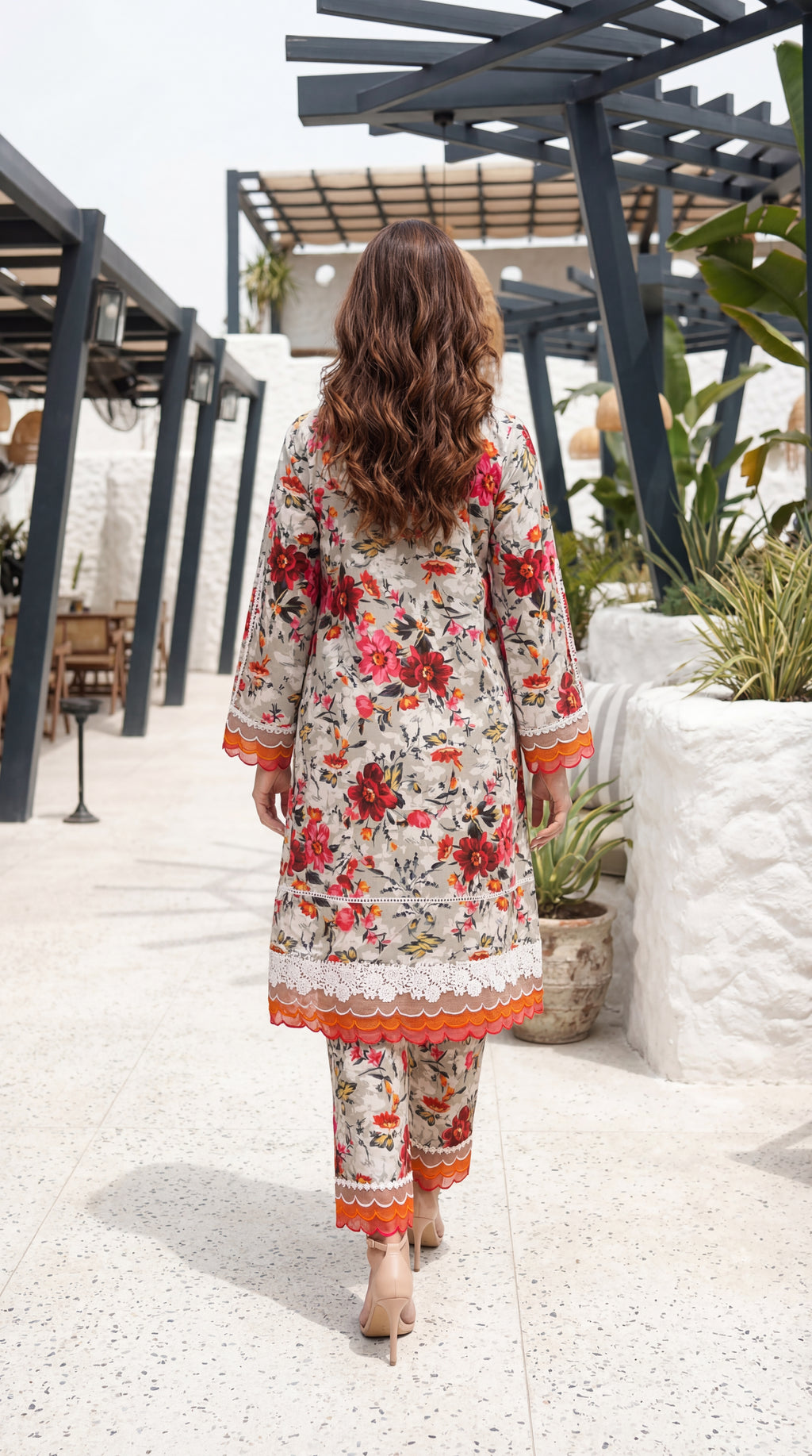 Woman in a floral dress walking outdoors with plants and structures in the background