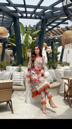 Woman in a floral outfit sitting in an outdoor setting with plants and furniture.