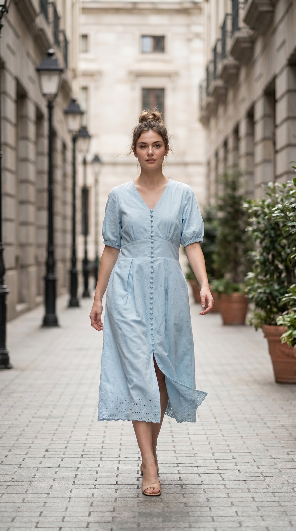 Woman in a light blue dress walking down a street with buildings and plants in the background