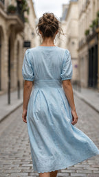 Woman in a light blue dress walking down a cobblestone street.
