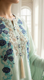 Light green embroidered garment with blue floral patterns and tassels, worn by a person.