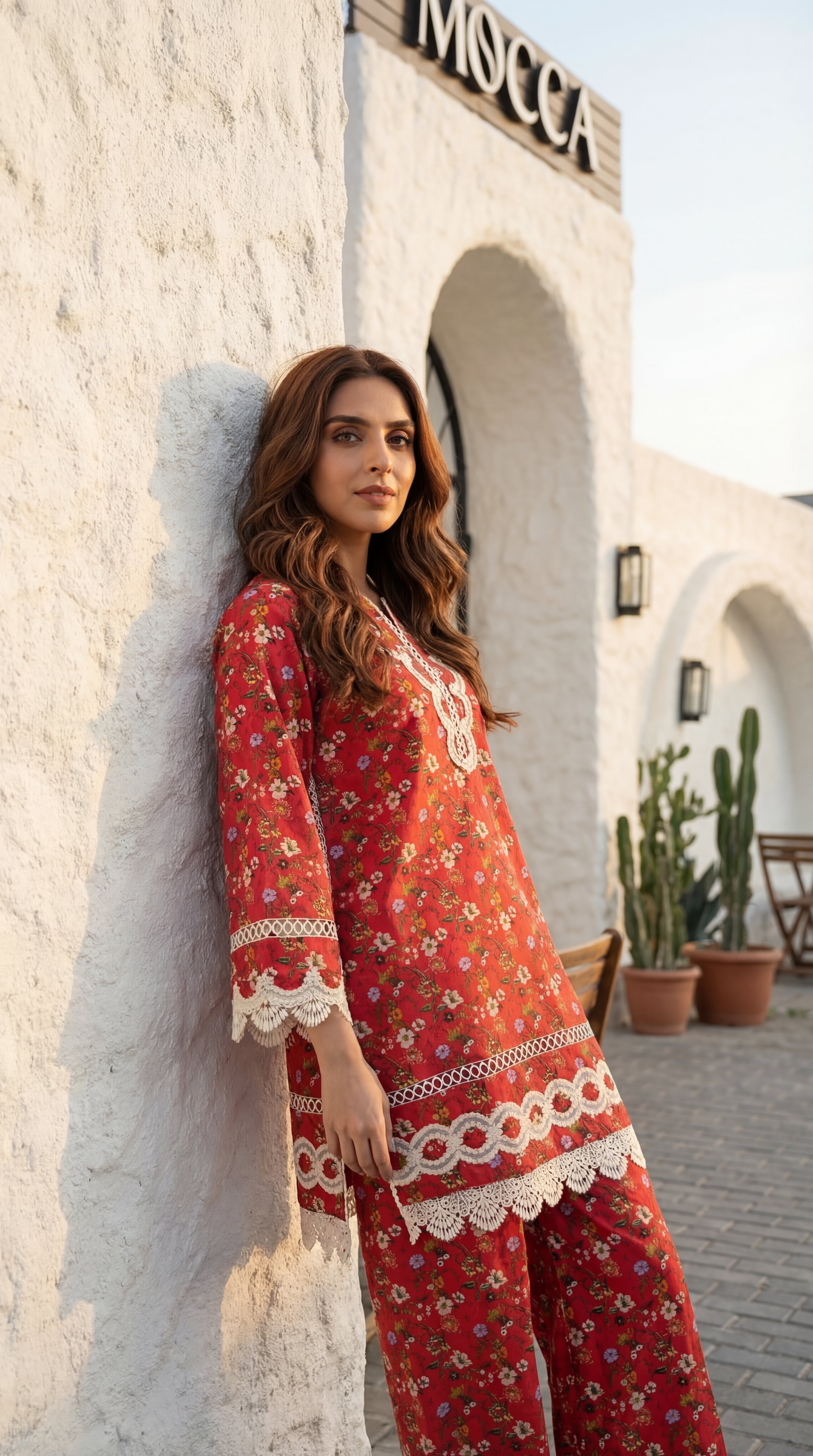 Woman in a red floral dress standing against a white wall with 'Moschino' branding.