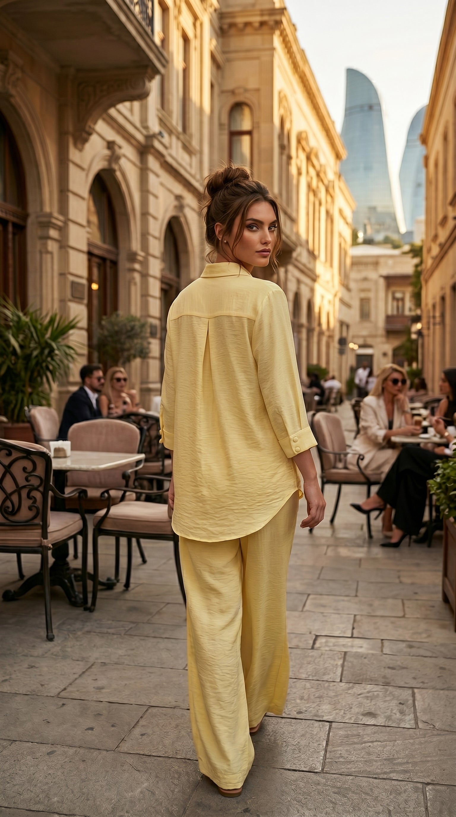 Woman in a yellow outfit walking on a city street with buildings and people in the background.
